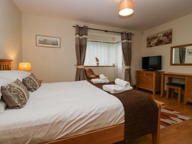 A bedroom with a double bed and folded towels by the window with curtains a TV on a dresser and a dressing table at Blue Hill House in Ambleside