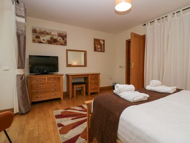 A bedroom with a bed covered with white and brown linens with rolled towels on it a wooden dresser with a television and a dressing table with a mirror at Blue Hill House Ambleside