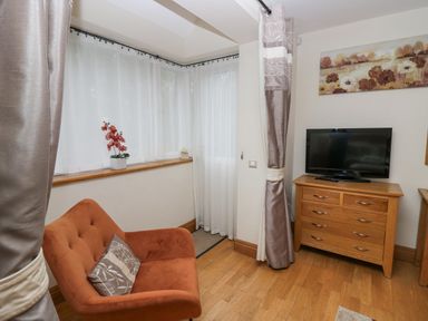 A corner of a living room with an orange armchair and a wooden dresser with a television on top at Blue Hill House in Ambleside