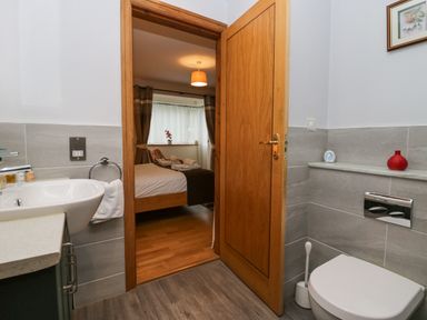 A bathroom with sink and toilet looking into a bedroom with a bed and curtains at Blue Hill House Ambleside