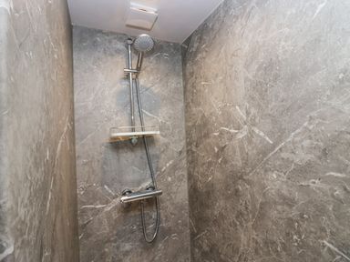 A shower area with grey marble walls a chrome showerhead and a small white shelf at Blue Hill House in Ambleside