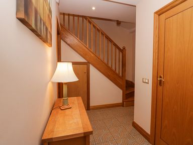 A hallway with wooden stairs a wooden table with a lamp a closed wooden door and tiled floor at Blue Hill House in Ambleside