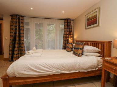A bedroom with a wooden bed frame white bedding rolled towels bedside table and curtains at Blue Hill House in Ambleside