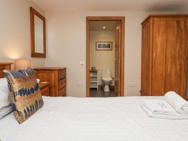 A bedroom with a bed white linens a wooden wardrobe and shelves and a view into a bathroom with a toilet at Blue Hill House in Ambleside