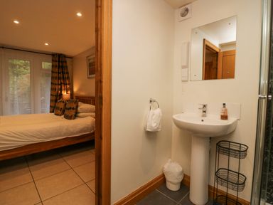 A bedroom with a wooden bed and patterned pillows next to a bathroom with a sink and mirror at Blue Hill House Ambleside
