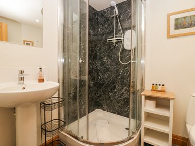 A bathroom with a corner shower enclosure a pedestal sink a small shelving unit and a framed picture on the wall at Blue Hill House in Ambleside