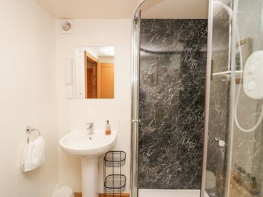 A bathroom with a white sink and mirror next to a shower with black marble walls at Blue Hill House in Ambleside