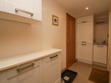 A utility room with white cabinets a wooden door a small sink and tiled floor at Blue Hill House Ambleside