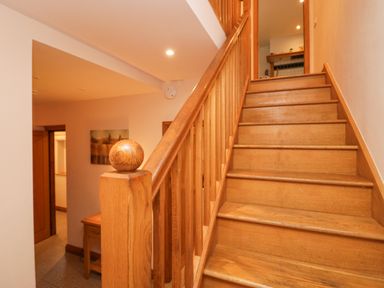A wooden staircase with handrail and a hallway with a table and wall art at Blue Hill House in Ambleside
