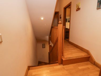 An indoor wooden staircase with a banister leading down and hallway entrance with wooden flooring at Blue Hill House in Ambleside