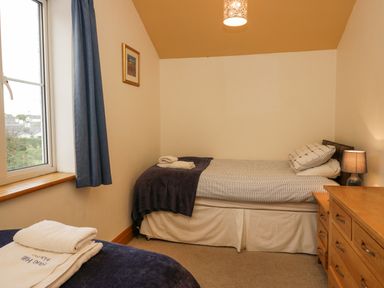 A bedroom with two beds a wooden dresser a window with blue curtains and a bedside lamp at Blue Hill House in Ambleside