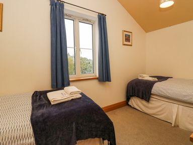 A bedroom with two single beds with folded towels on top and a window with blue curtains at Blue Hill House in Ambleside