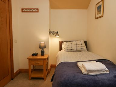A bedroom with a single bed a wooden bedside table with a lamp and a wall-mounted reading light at Blue Hill House in Ambleside