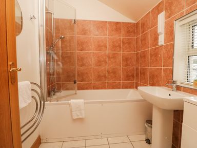 A bathroom with a bathtub shower combination and a sink next to a window at Blue Hill House in Ambleside