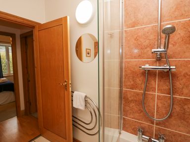 A bathroom with a showerhead and tiled wall next to an open wooden door showing part of a bedroom at Blue Hill House in Ambleside