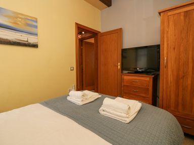 A bedroom with a bed covered in white and gray bedding towels on the bed wooden wardrobe and dresser with a television on top at Blue Hill House in Ambleside