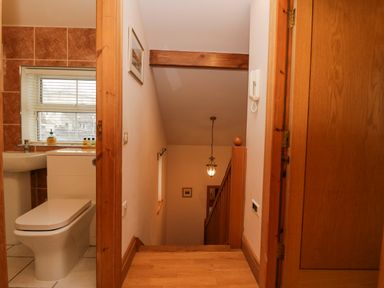 A hallway with wooden flooring and stairs leading down with a bathroom visible on the left at Blue Hill House in Ambleside
