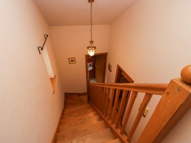 A wooden staircase with railing leading down to a hallway with an open door showing a sink at Blue Hill House in Ambleside