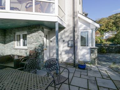 An outdoor patio area with metal table and chairs stone wall and two white doors at Blue Hill House in Ambleside