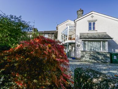 A front view of a house with stone and white exterior walls and a red shrub in the foreground at Blue Hill House in Ambleside