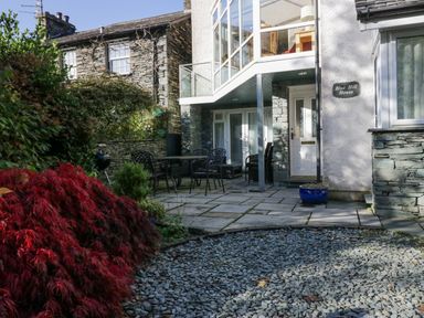 A patio area with black metal table and chairs outside a stone and white house named Blue Hill House in Ambleside
