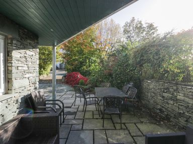 An outdoor patio with a table and chairs surrounded by stone walls and trees at Blue Hill House in Ambleside