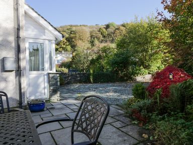 A patio with metal outdoor furniture next to a door and a garden with trees and shrubs at Blue Hill House in Ambleside