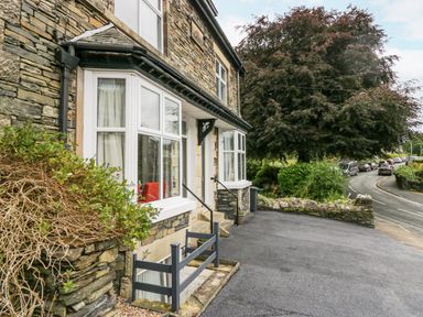 Stone house exterior with white windows and a paved driveway near a road with cars and trees at Park Beck 3 in Windermere