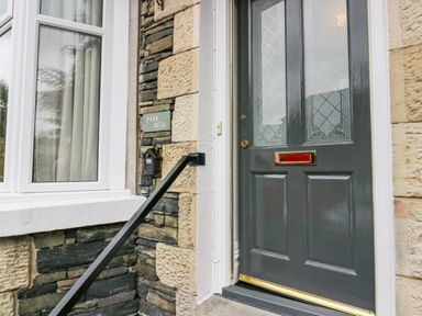 A front door with frosted glass panels and a mailbox on a stone wall next to a window at Park Beck 3 in Windermere