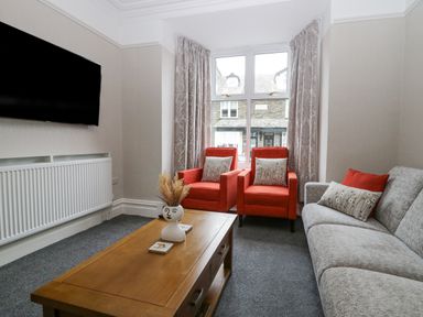 A living room with two red armchairs a gray sofa a wooden coffee table and a wall-mounted tv at Park Beck 3 in Windermere