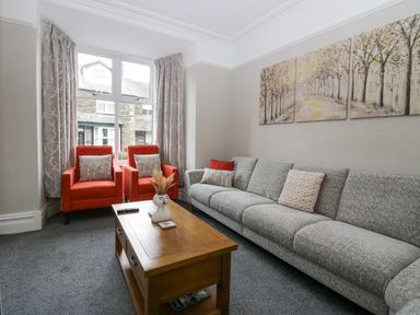 A sitting room with a grey sofa two orange armchairs a wooden coffee table and a triptych tree painting on the wall at Park Beck 3 in Windermere