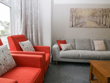 A living room with red armchairs a grey sofa with cushions a wooden coffee table and a three-panel tree painting at Park Beck 3 in Windermere