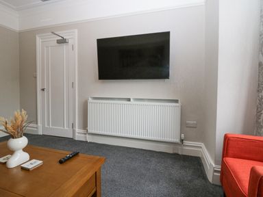 A wall mounted television above a white radiator with a wooden coffee table and a red chair in a living room at Park Beck 3 in Windermere