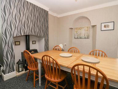 A dining room with a wooden table and six chairs near a small stove and patterned wallpaper at Park Beck 3 in Windermere