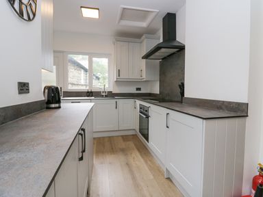 A kitchen with white cabinets a stove a black kettle and a window at Park Beck 3 Windermere