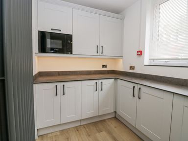 A kitchen with white cabinets a built in microwave and a window with blinds at Park Beck 3 in Windermere