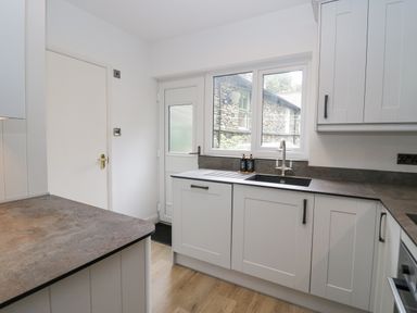 A kitchen with white cabinets a countertop window above the sink and a door showing an outside stone wall at Park Beck 3 in Windermere