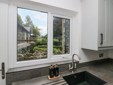 A kitchen sink with soap dispensers beneath a window showing a garden view at Park Beck 3 in Windermere