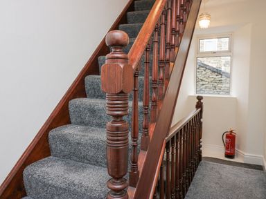 A carpeted staircase with wooden banister and a window with a fire extinguisher below at Park Beck 3 in Windermere