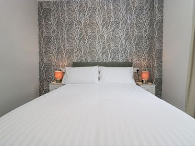 A bedroom with a double bed two bedside tables with lamps and tree patterned wallpaper at Park Beck 3 in Windermere