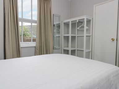 A bedroom with a bed white shelving unit with hangers a window with beige curtains and a full length mirror at Park Beck 3 in Windermere