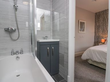 A bathroom with a bathtub shower and sink cabinet next to a bedroom with a bed and nightstand at Park Beck 3 in Windermere