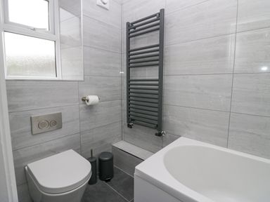 A bathroom with a toilet, toilet paper holder, heated towel rail, window, trash bin, toilet brush, and bathtub at Park Beck 3 in Windermere