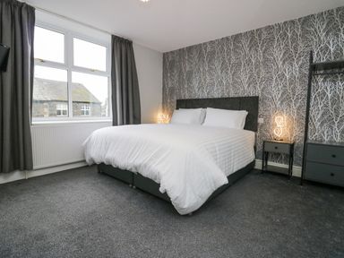 A bedroom with a large bed white bedding bedside tables with lamps patterned wallpaper and gray curtains at Park Beck 3 in Windermere