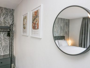 A bedroom with patterned wallpaper a round mirror two framed pictures and a black clothing rack at Park Beck 3 in Windermere