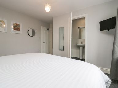 A bedroom with a bed a wall-mounted television an open door leading to a bathroom curtains and framed pictures on the wall at Park Beck 3 in Windermere