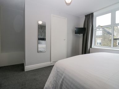 A bedroom with a bed a wall mirror a closed door a wall-mounted television and a window with curtains at Park Beck 3 in Windermere