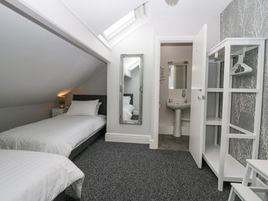 A bedroom with two beds a bedside table with lamp a tall mirror an open door to a bathroom and a white shelving unit with hangers at Park Beck 3 in Windermere