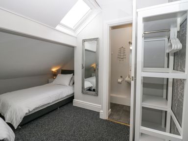 A bedroom with a single bed nightstand and lamp a wall mirror an open door to a bathroom and an open closet with hangers at Park Beck 3 in Windermere