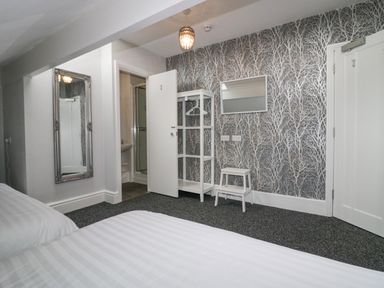 A bedroom with two beds a patterned wallpaper a mirror a white wardrobe and a small white stool at Park Beck 3 in Windermere